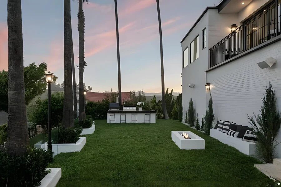 The Fire Pit Lawn &mdash; A linear fire feature and outdoor kitchen set beneath palms at dusk.