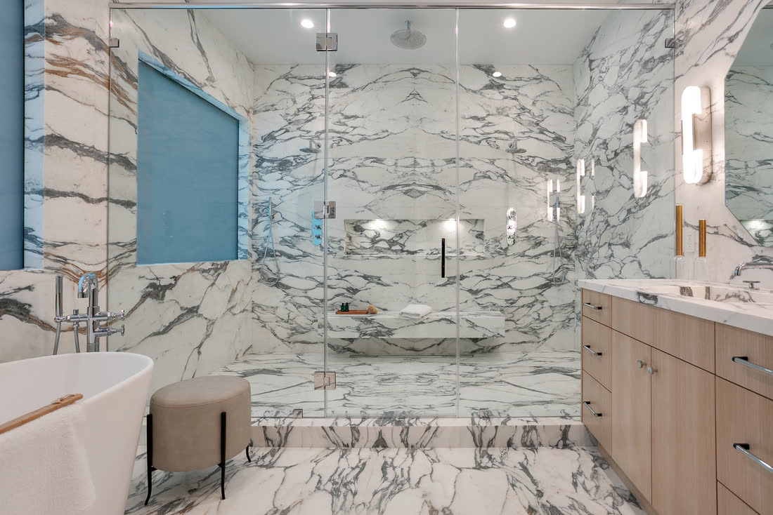Primary bathroom remodel with book-matched marble shower surround, frameless glass enclosure, built-in niche and bench, and freestanding tub